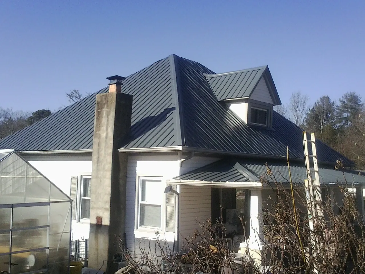 Dark blue standing seam metal roof on a white farmhouse with dormer — Slate & Tile Roof Repair by Roofing Brothers in Cokeville