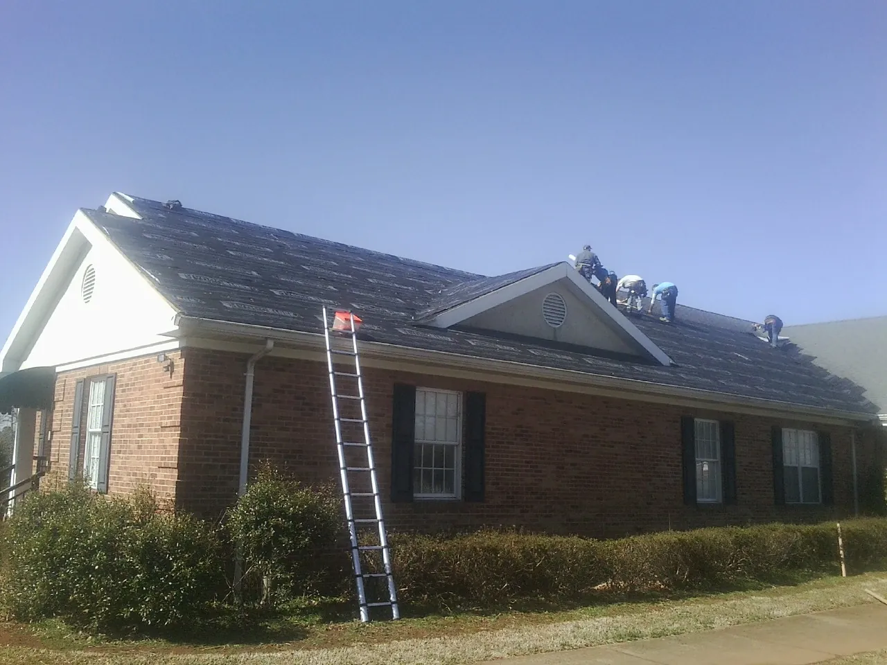 Crew tearing shingles off a brick ranch roof with a ladder set — Metal Roof Repair work by our crew in Cokeville