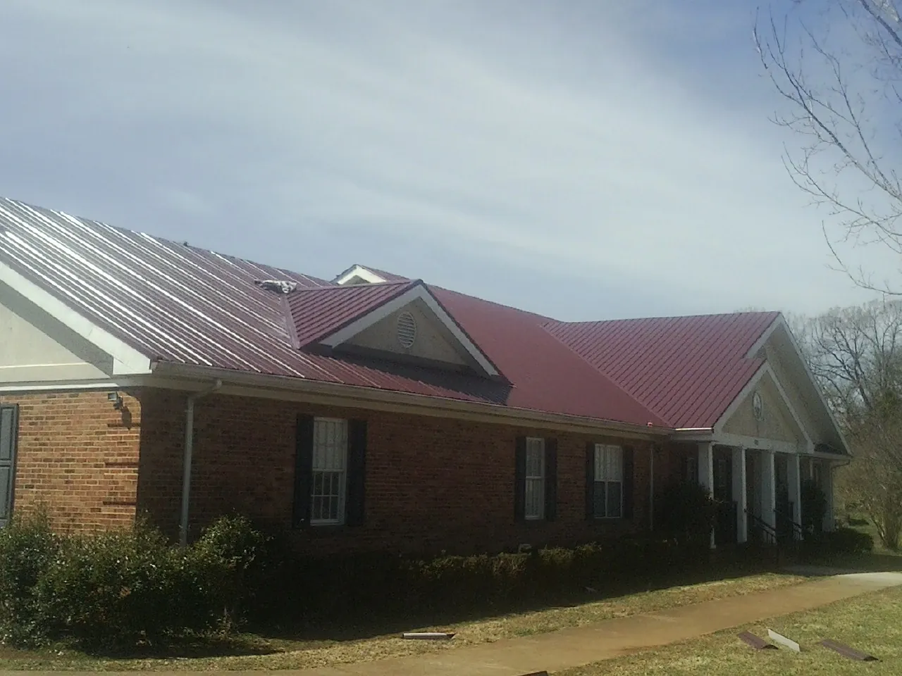 Red metal roof with gabled entries on a long brick building, from a Hail Damage Roof Repair job in Cokeville