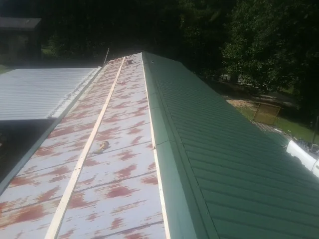 Old rusted panels beside newly installed green metal roofing — Wind Damage Roof Repair by Roofing Brothers in Cokeville