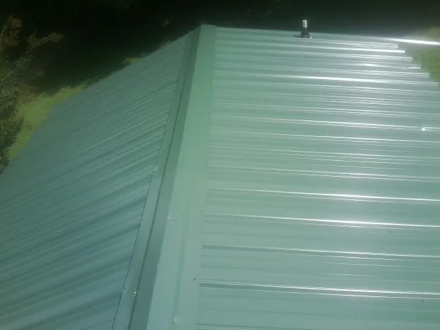New green metal panels meeting at the ridge of a roof — Flat Roof Repair work by our crew in Cokeville