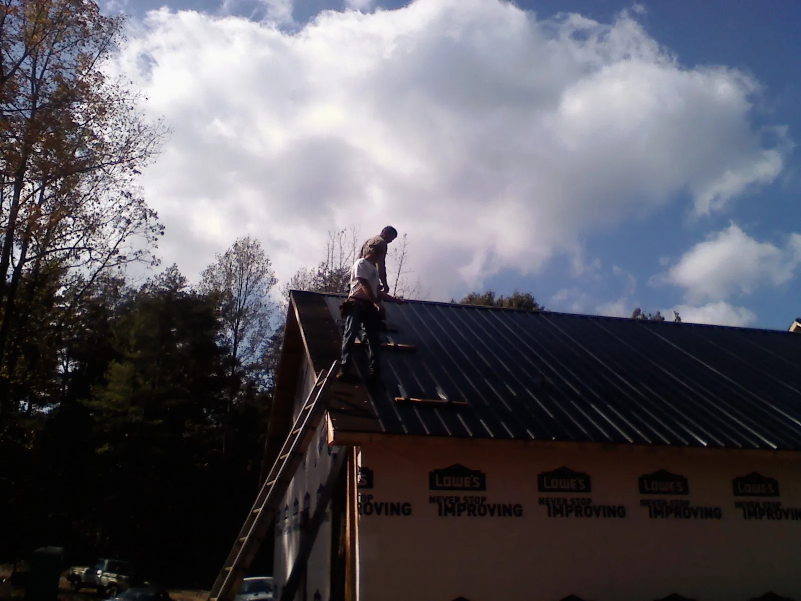 Roofer fastening dark metal panels high against a cloudy sky, from a Roof Inspection job in Cokeville