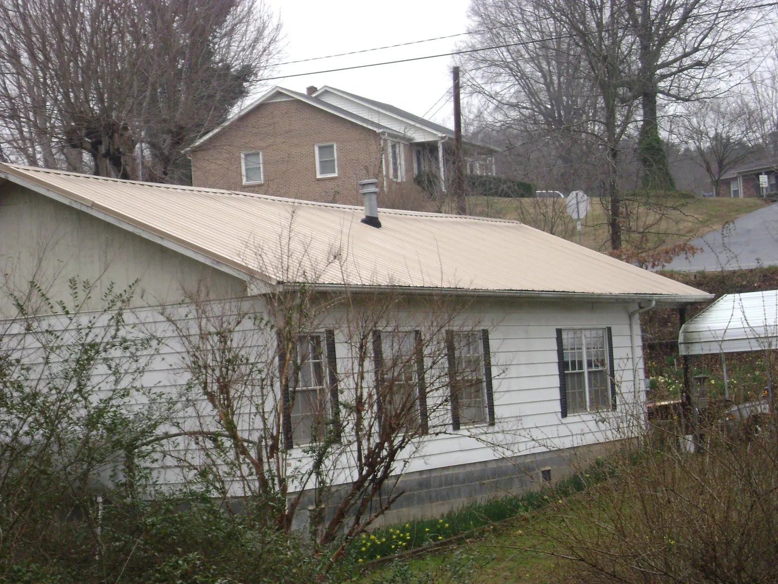 Tan metal roof on a white sided house set into a hillside — Commercial Roofing by Roofing Brothers in Cokeville